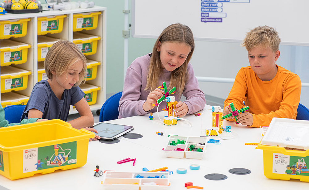 Schüler sitzen am Tisch und bauen Lego-Modell auf