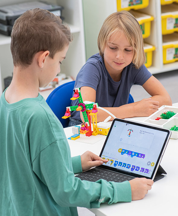 Schüler programmiert das Model am Tablet, anderer Schüler schaut dem Modell zu