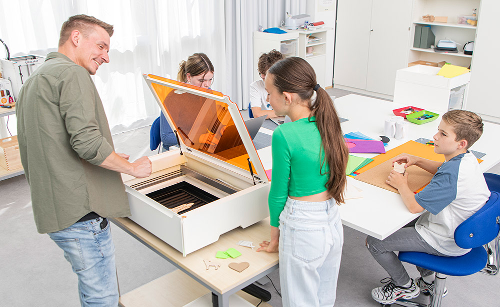 Kinder und ein Lehrer sitzen/stehen um einen Tisch mit Laser