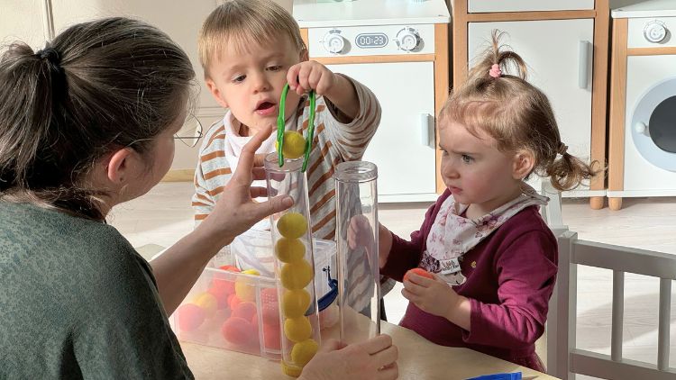 Ein Kind sortiert Pompons farblich passend in Röhren